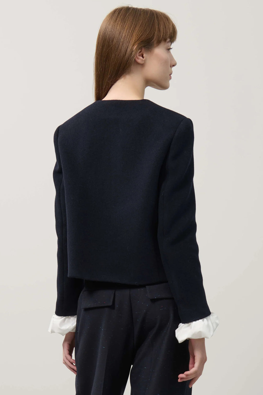 Person wearing a navy blazer and dark pants with a white shirt underneath on a light gray background