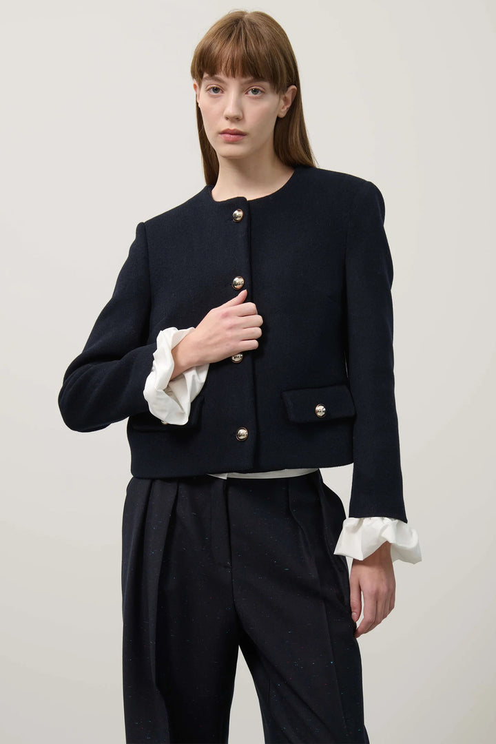 Woman wearing a dark blue jacket with white trim on a plain background