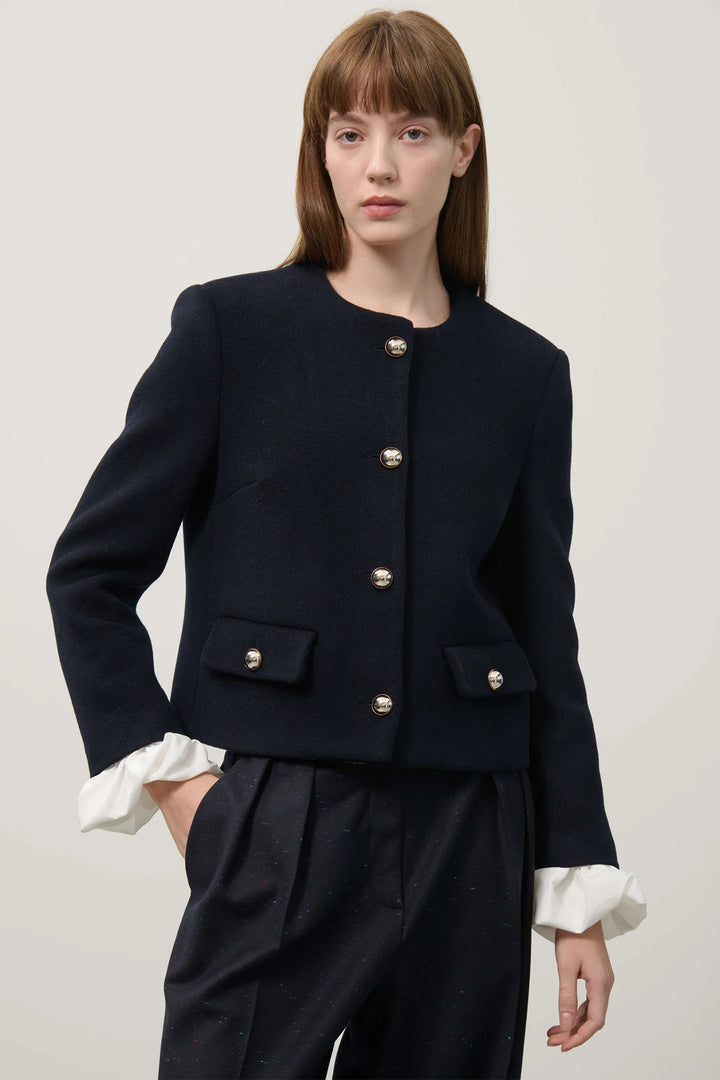 Woman wearing a dark blue jacket with white cuffs and trim on a plain background