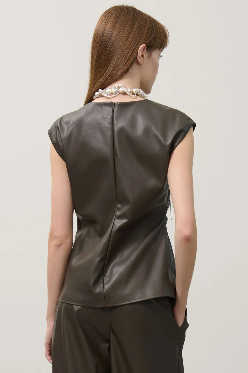 Woman wearing a khaki leather sleeveless top against a plain background