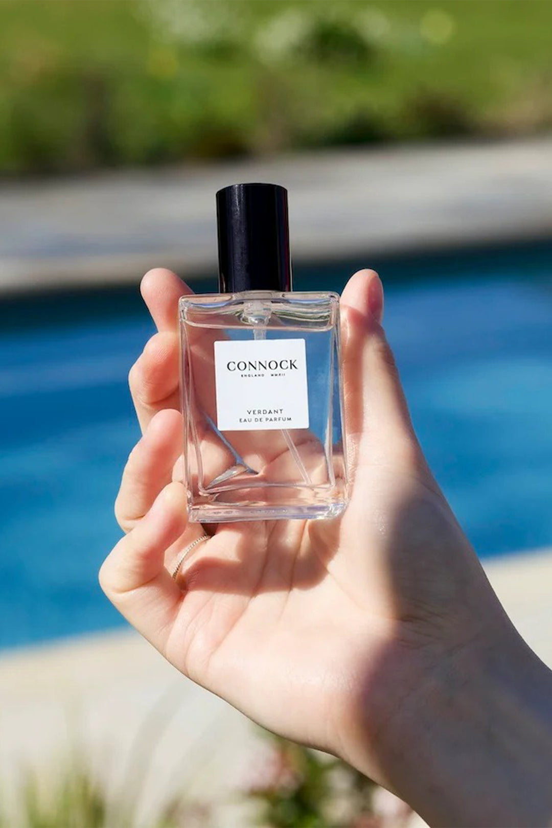 Hand holding a Conndock perfume bottle with a pool in the background
