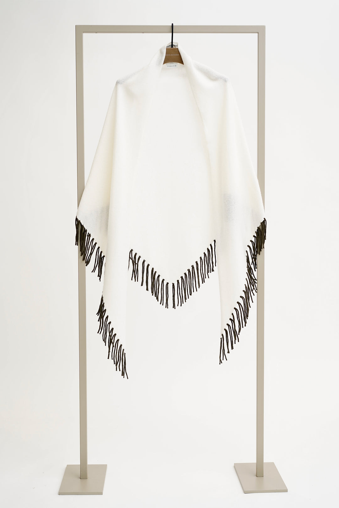 White poncho with black fringe on a stand against a white background