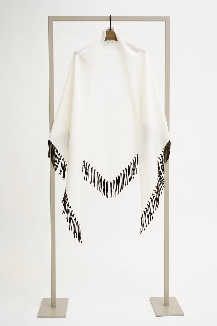 White poncho with black fringe on a stand against a white background