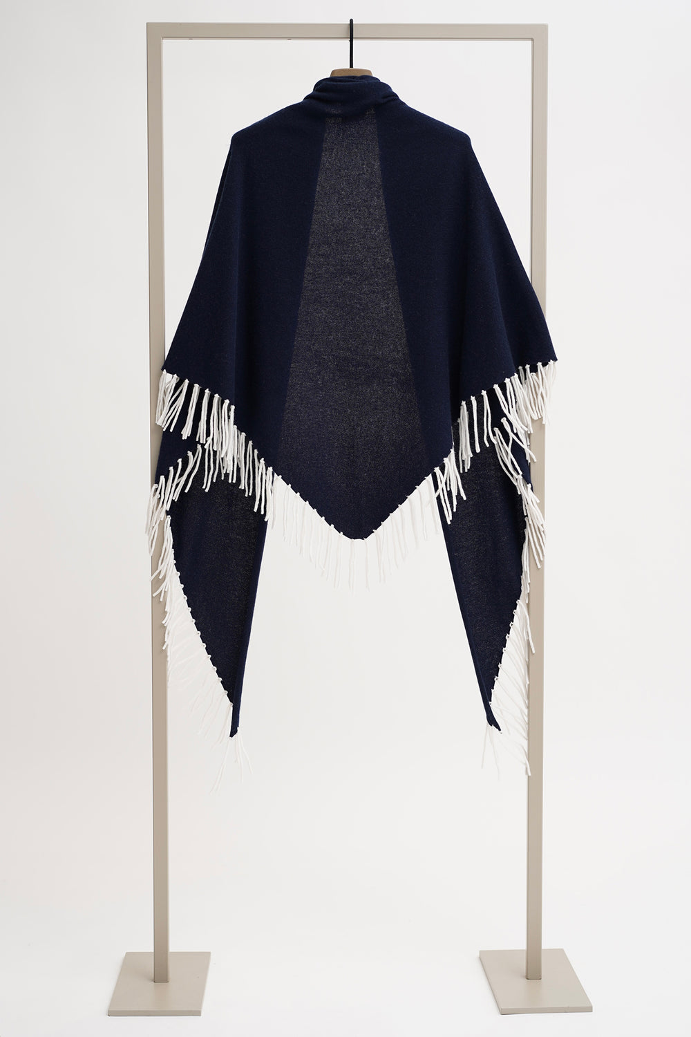 Navy blue poncho with white fringe on a stand against a white background