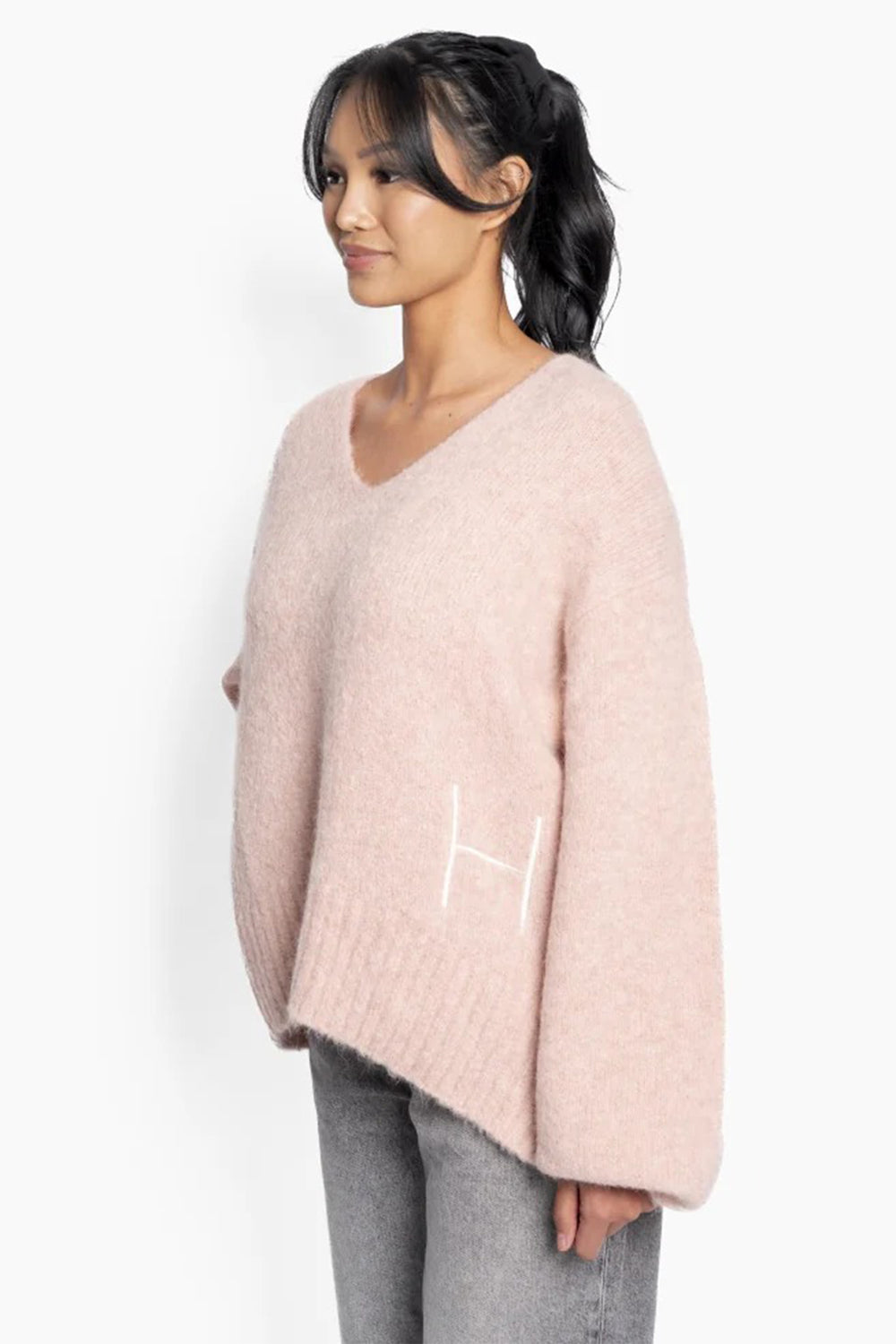 Woman wearing a light pink sweater with a logo on a white background
