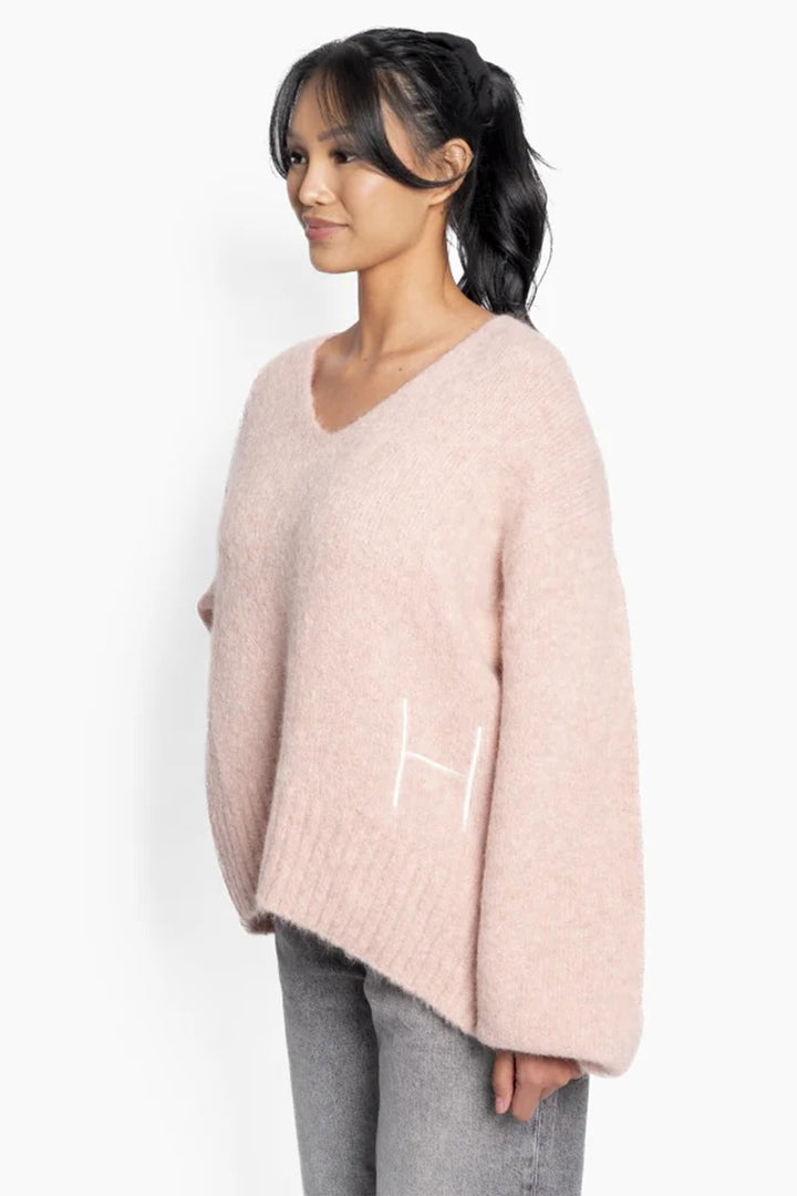 Woman wearing a light pink sweater with a logo on a white background