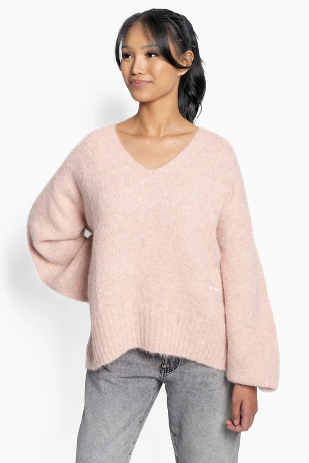 Woman wearing a light pink sweater and gray pants on a white background