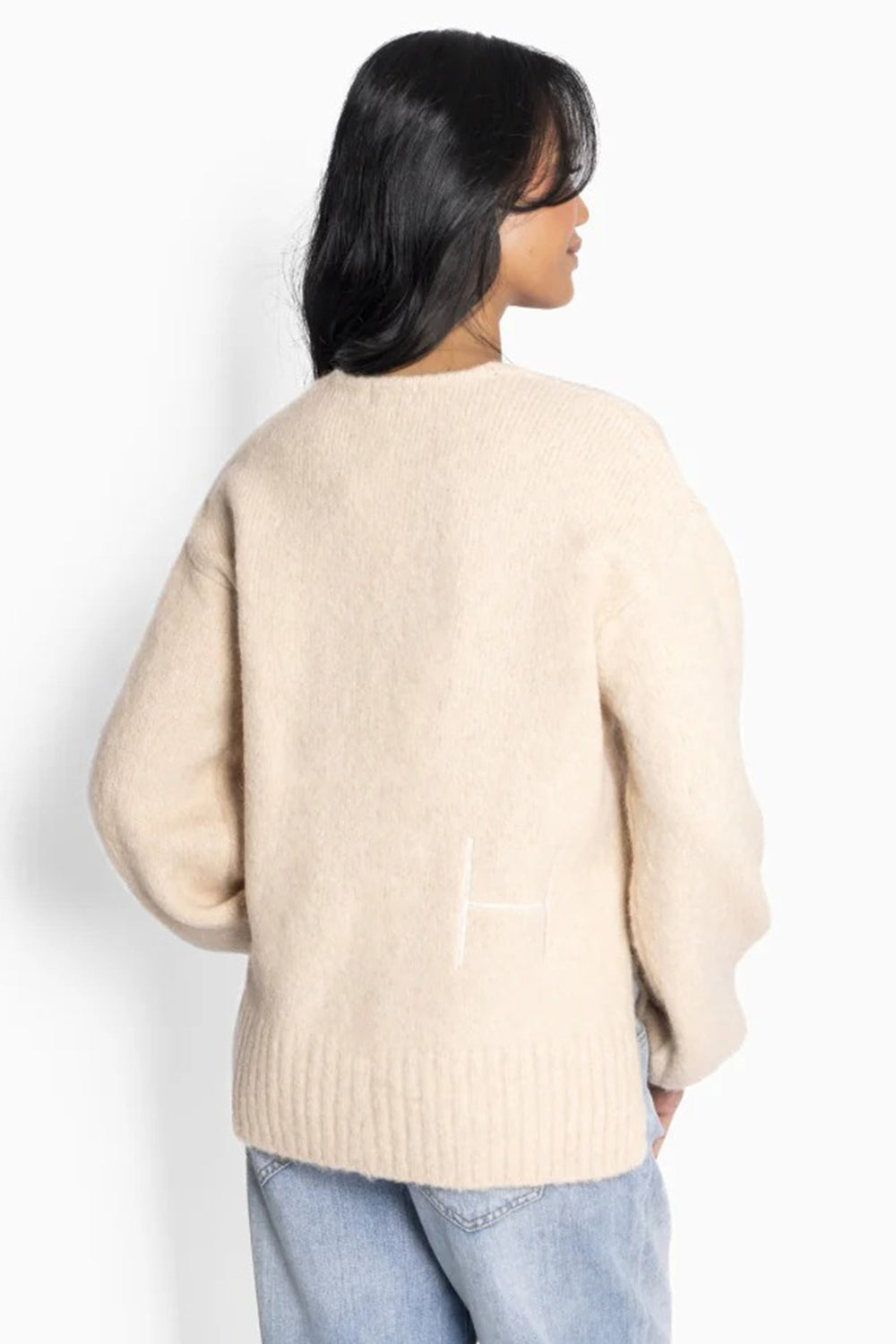 Person wearing a beige sweater and light blue jeans on a white background