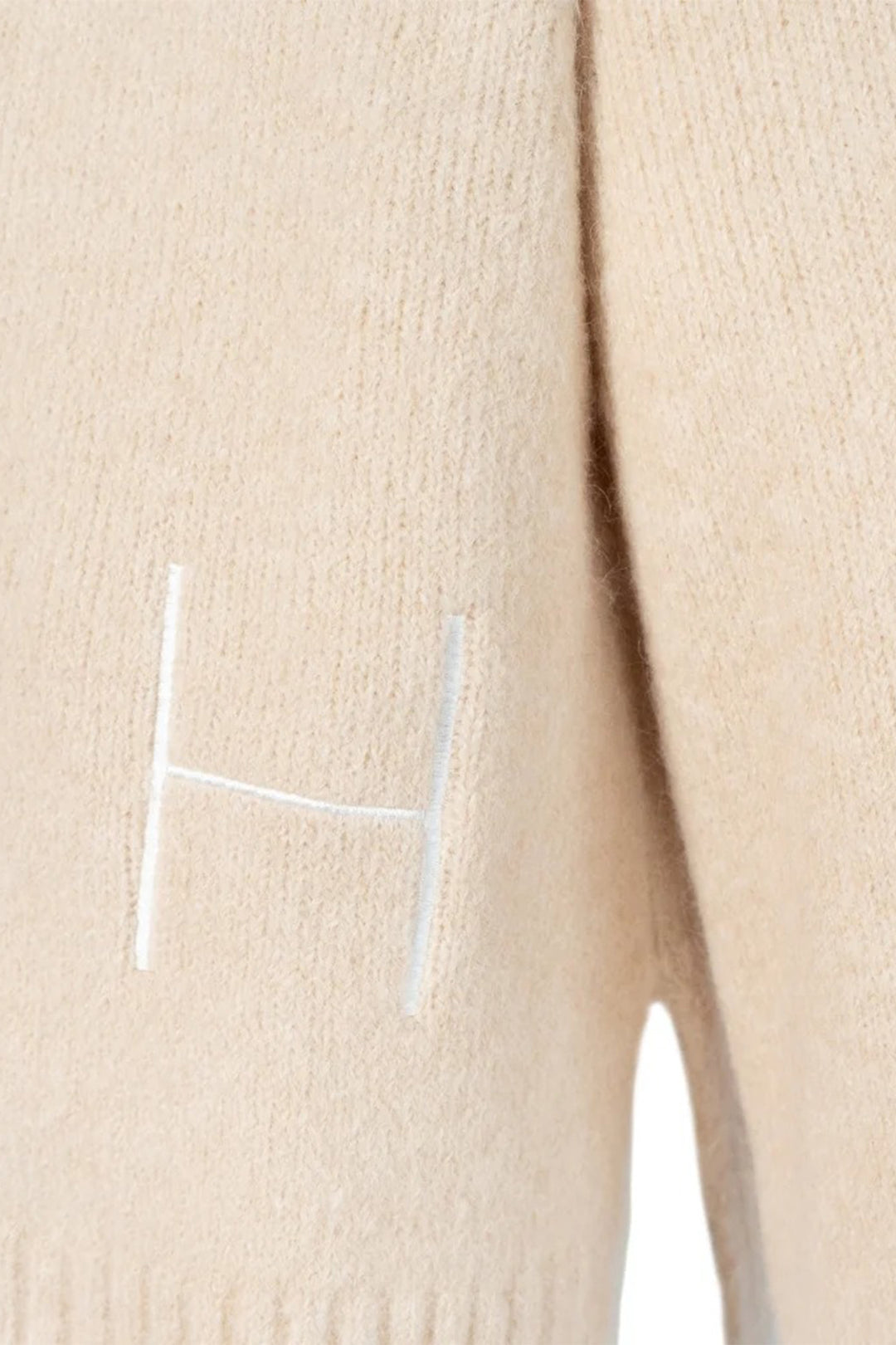 Beige sweater with a white 'H' logo on a beige background
