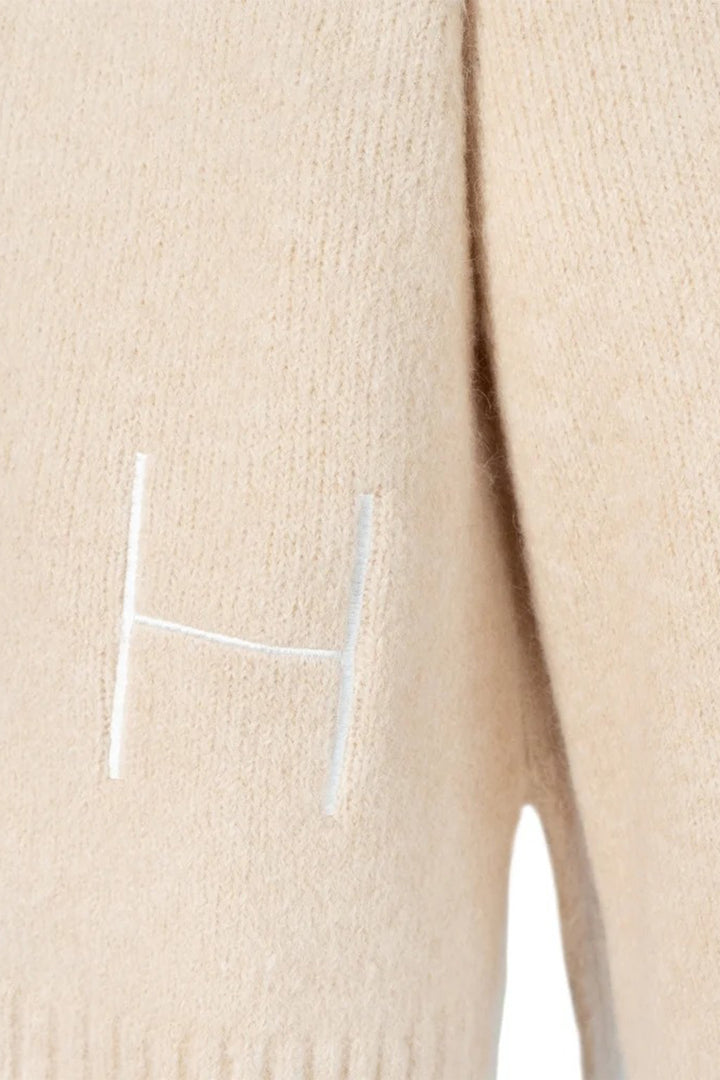 Beige sweater with a white 'H' logo on a beige background