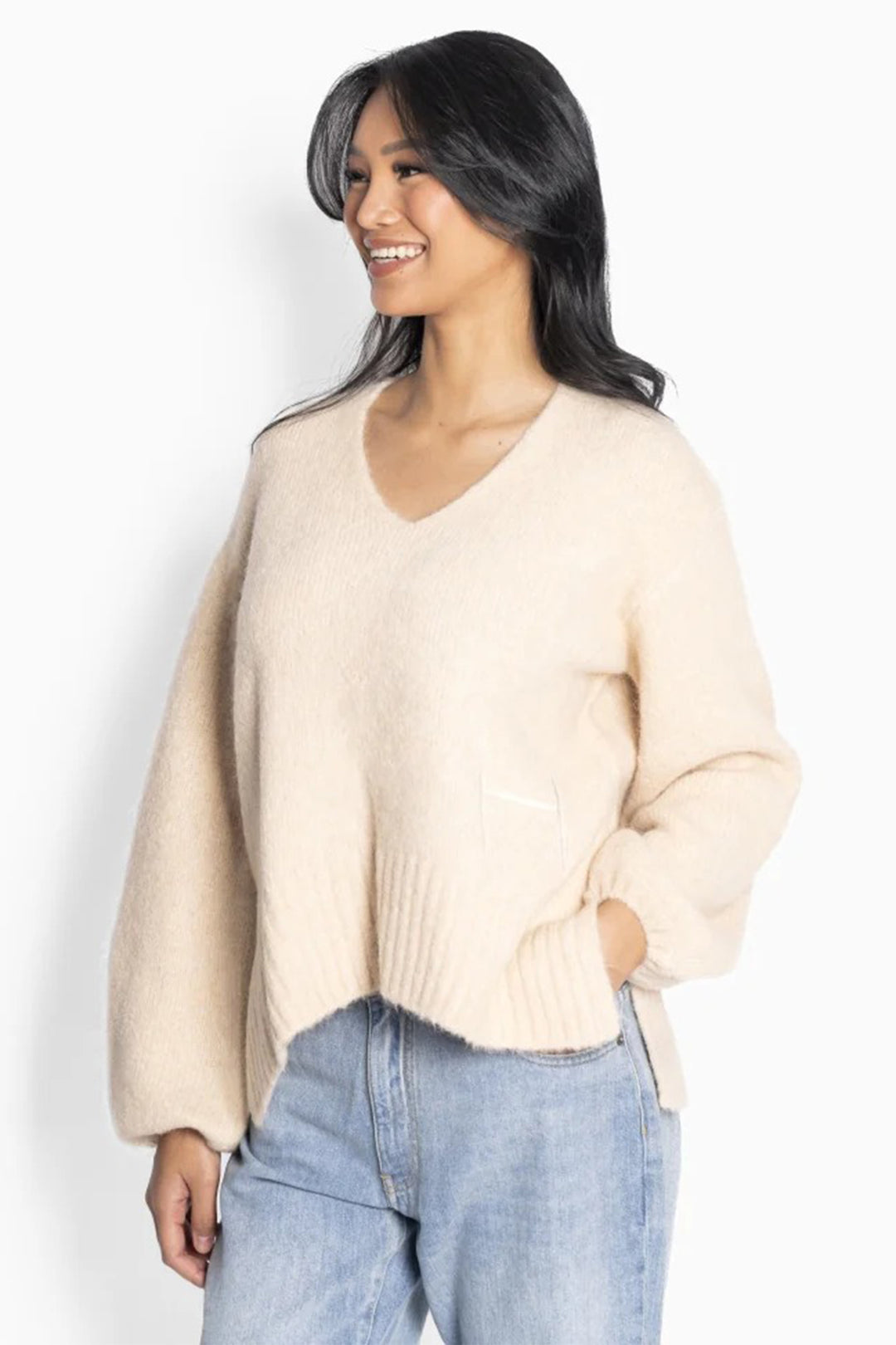 Woman wearing a beige sweater and blue jeans against a white background