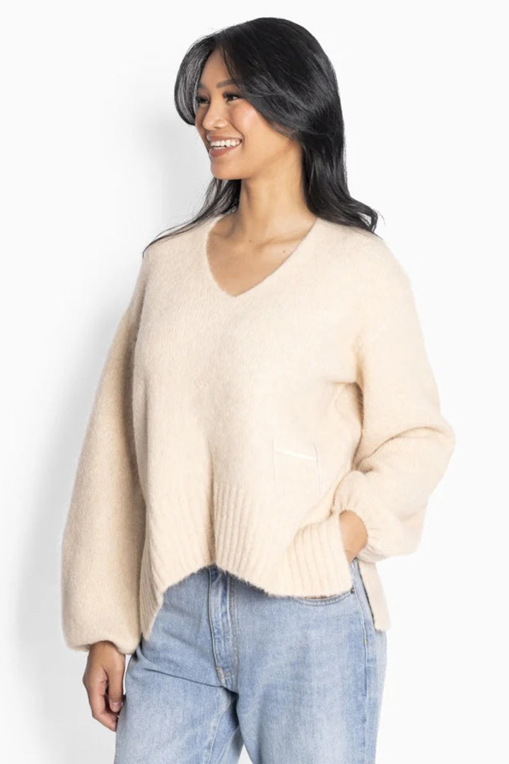 Woman wearing a beige sweater and blue jeans against a white background