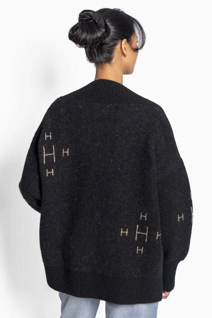 Person wearing a black sweater with gold symbols on a white background