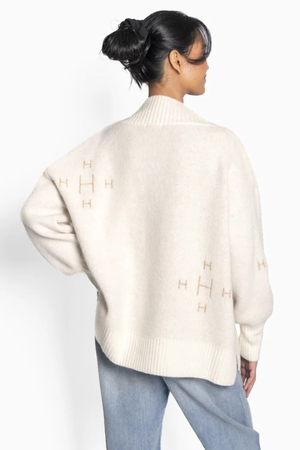 Person wearing a cream sweater with a logo on a white background