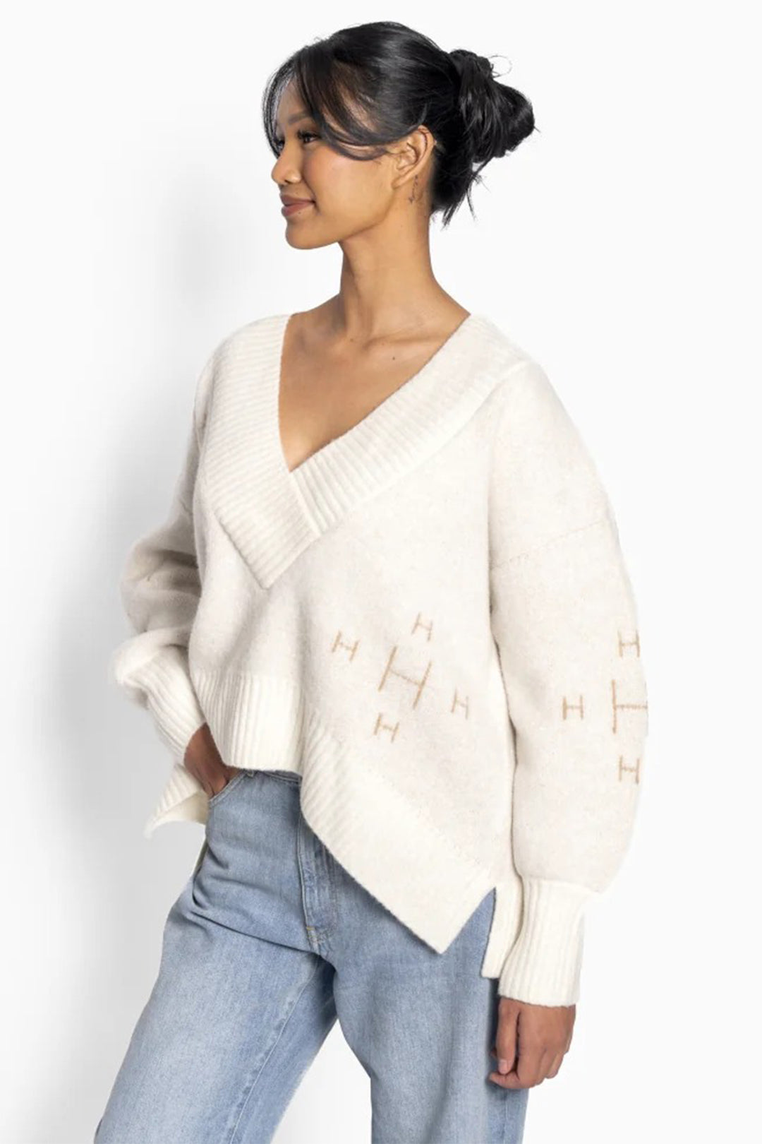 Woman wearing a cream sweater with a V-neck and light blue jeans on a white background