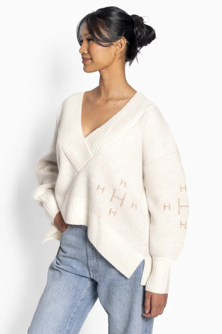Woman wearing a cream sweater with a V-neck and light blue jeans on a white background