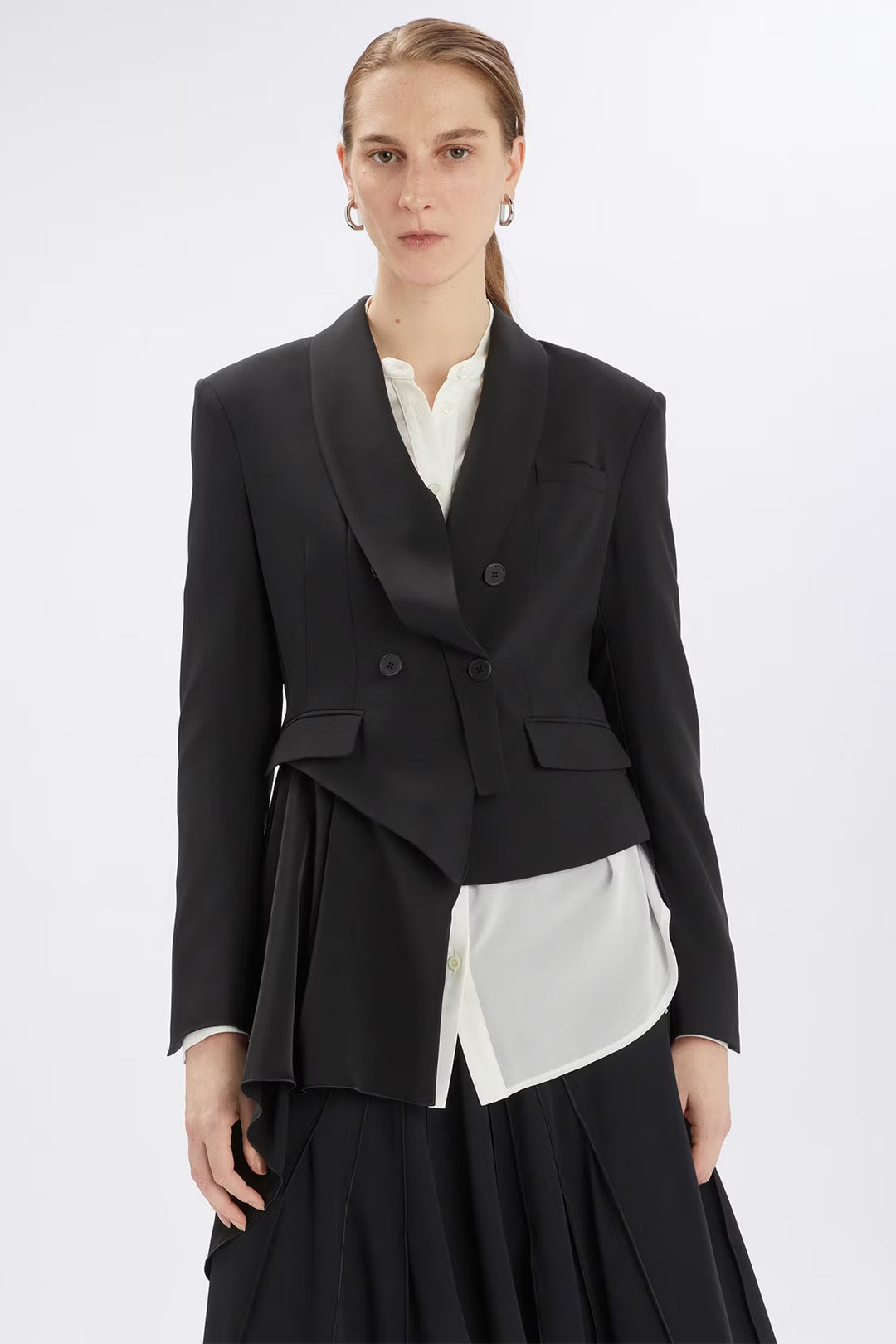Woman wearing a black blazer over a white shirt with a black skirt on a white background
