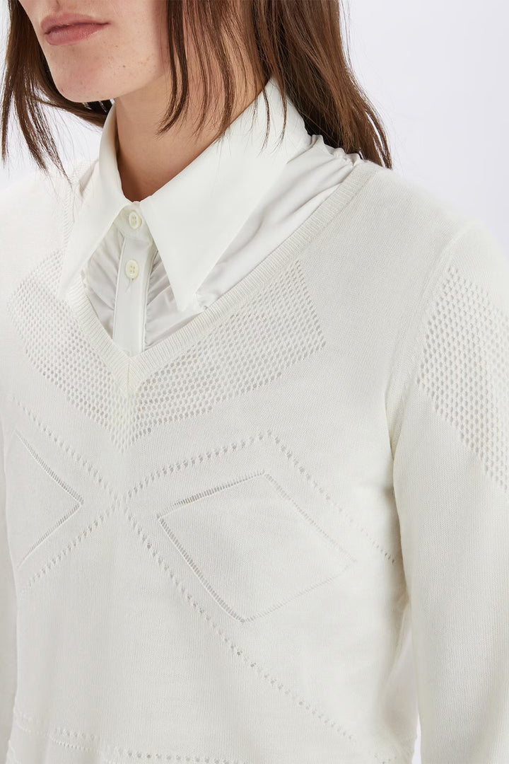 Close-up of a person wearing a white textured sweater over a collared shirt.