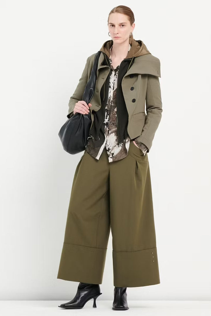 Woman wearing a green coat and wide-leg pants holding a black bag on a white background