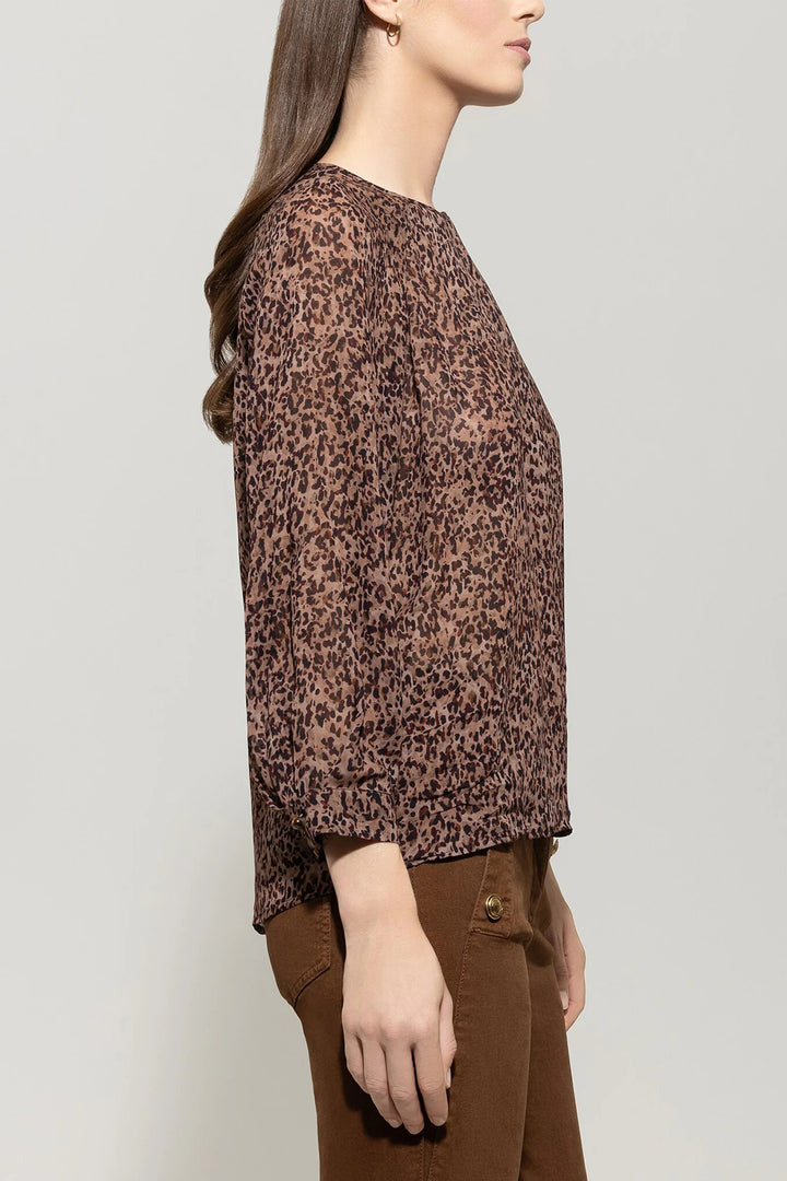 Woman wearing a brown patterned blouse and brown pants against a plain background