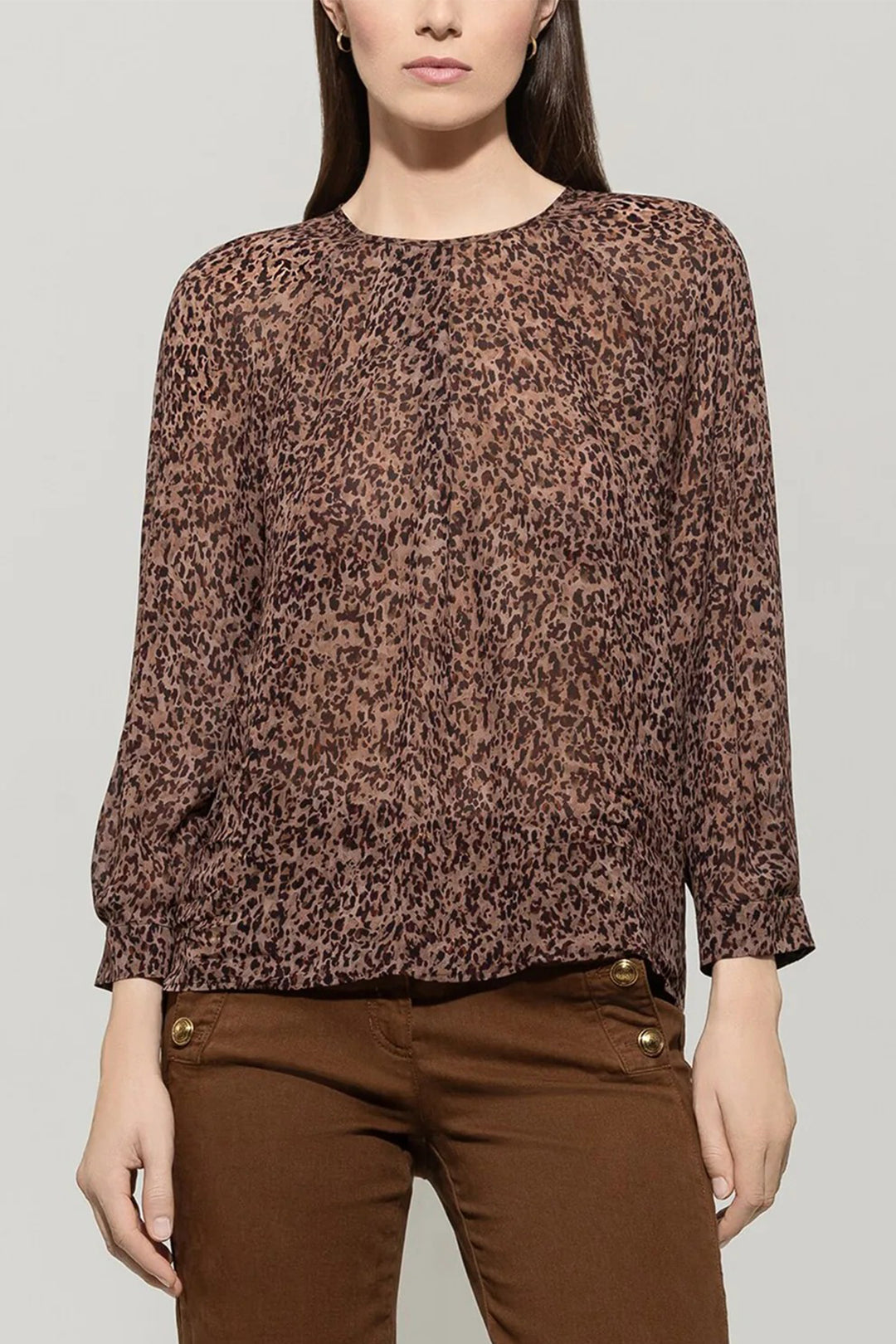 Woman wearing a brown leopard print top and brown pants on a gray background