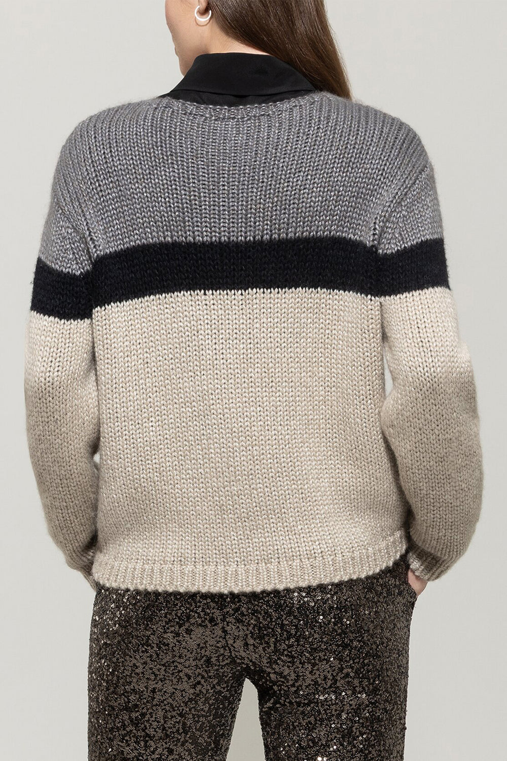 Person wearing a gray and beige sweater with a black stripe on a plain background