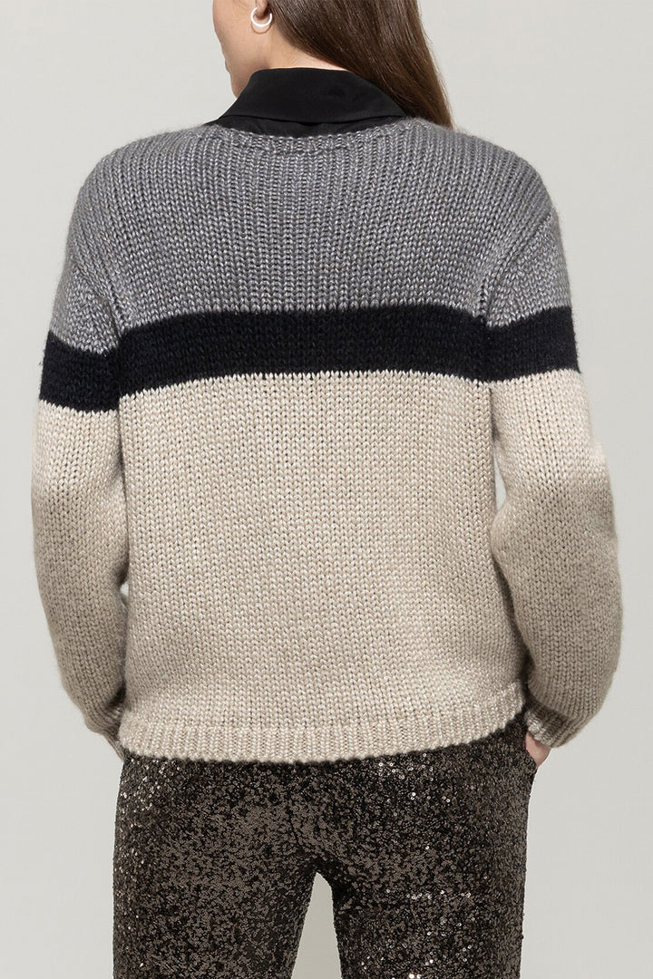 Person wearing a gray and beige sweater with a black stripe on a plain background