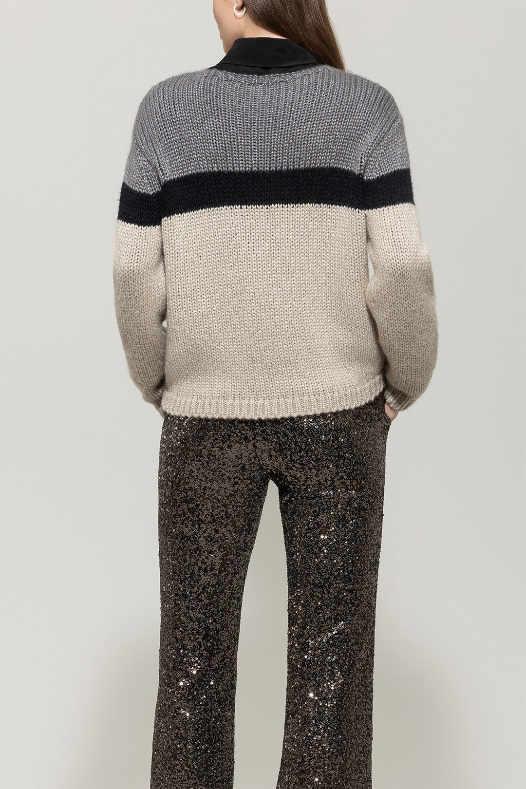 Person wearing a gray and beige sweater with black accents on a plain background
