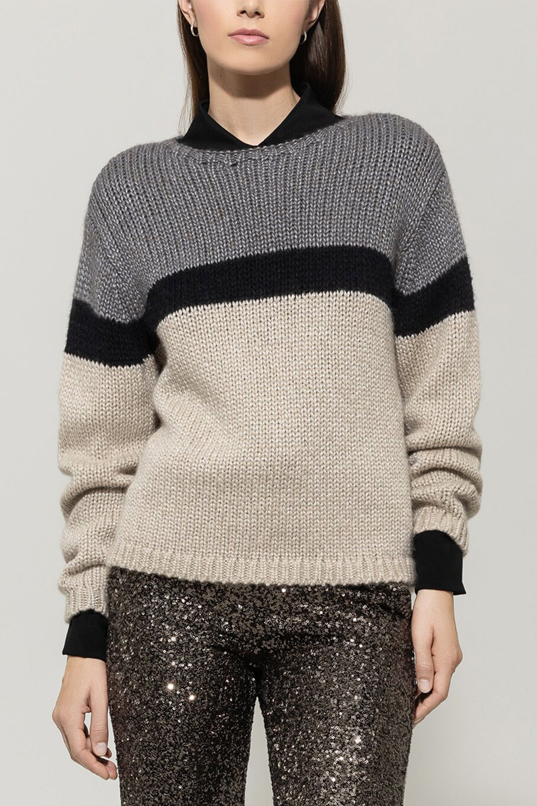 Person wearing a gray and black sweater with sequin pants on a plain background
