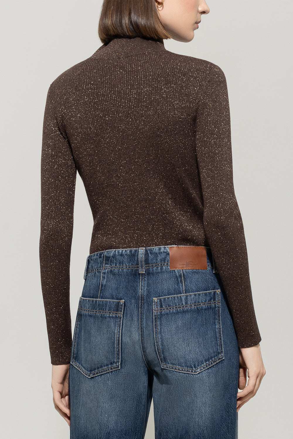 Person wearing a brown turtleneck sweater and blue jeans on a plain background