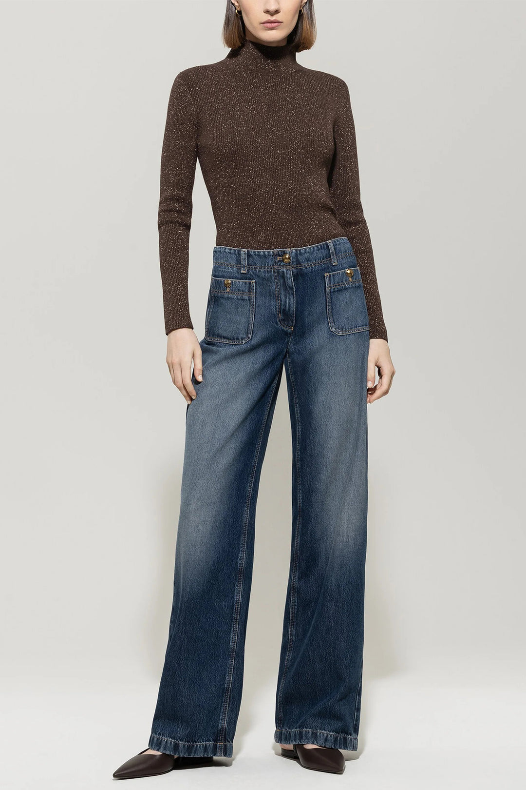 Person wearing a brown turtleneck sweater and blue jeans on a plain background