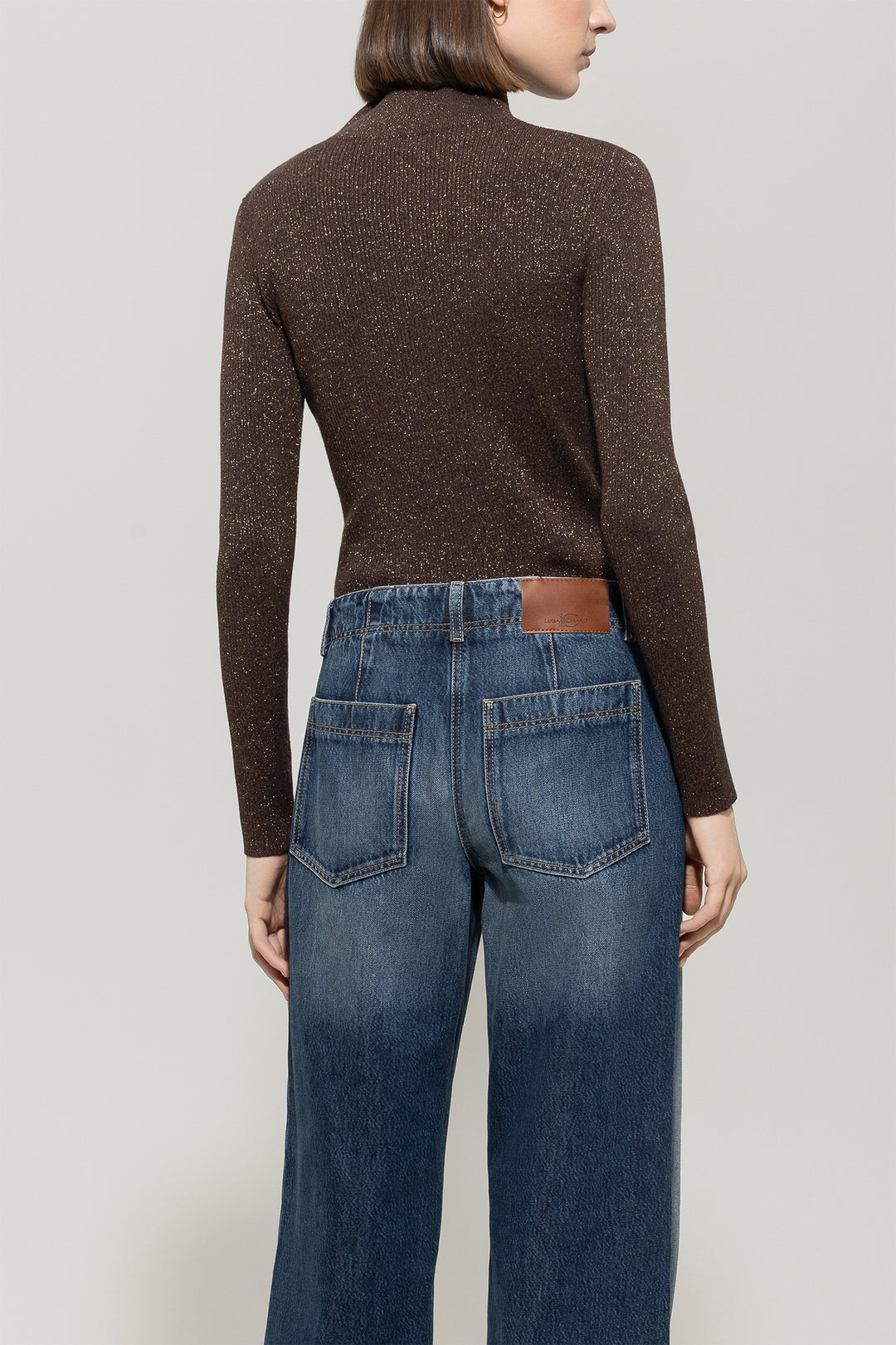 Person wearing a brown sweater and blue jeans on a plain background