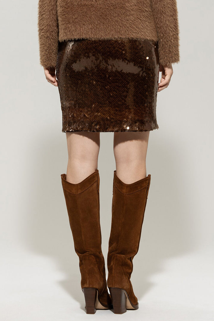 Person wearing a brown sequin skirt and knee-high brown boots on a white background
