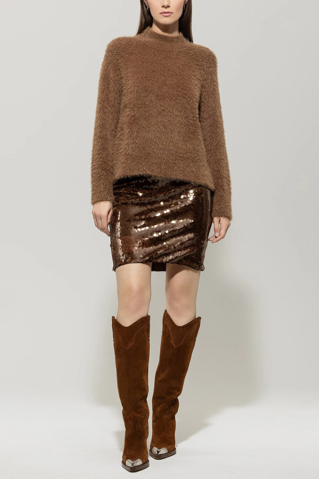 Person wearing a brown sweater, sequin skirt, and knee-high boots on a white background