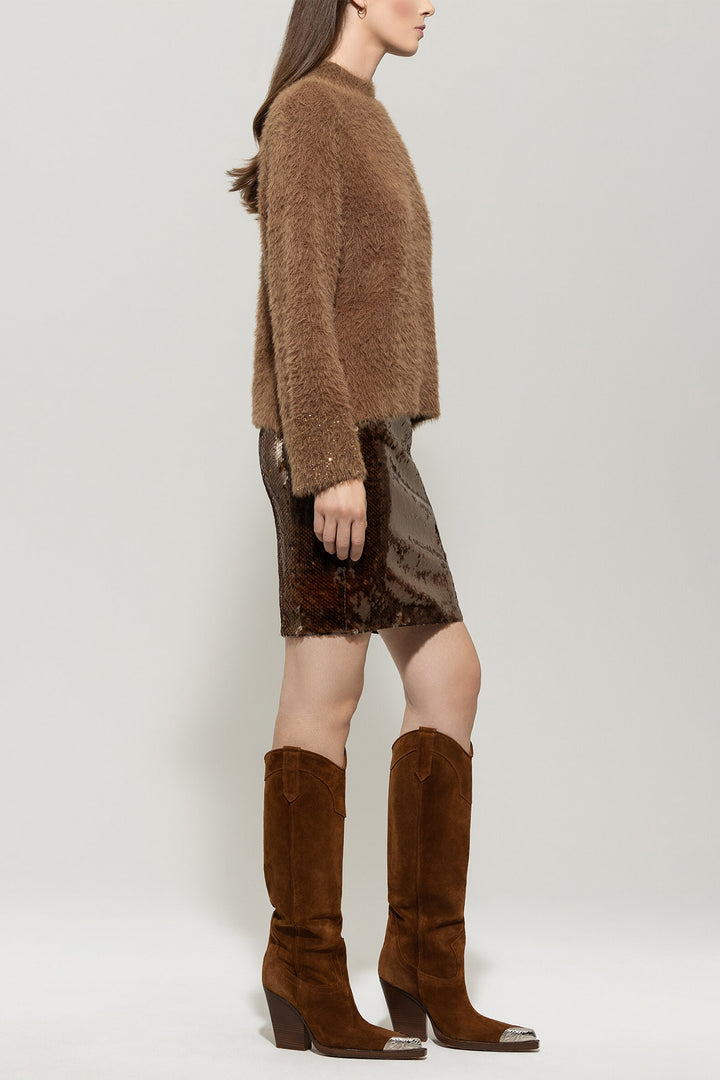 Woman wearing a brown fuzzy sweater, patterned skirt, and brown knee-high boots on a light gray background