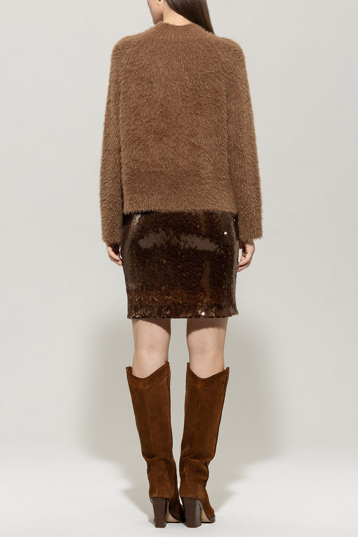 Person wearing a brown fuzzy sweater and skirt with knee-high brown boots on a white background