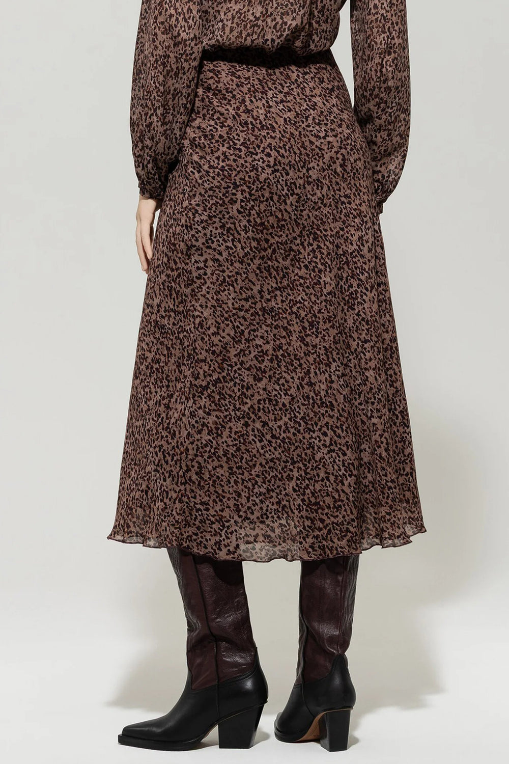 Person wearing a brown leopard print dress with black knee-high boots on a white background