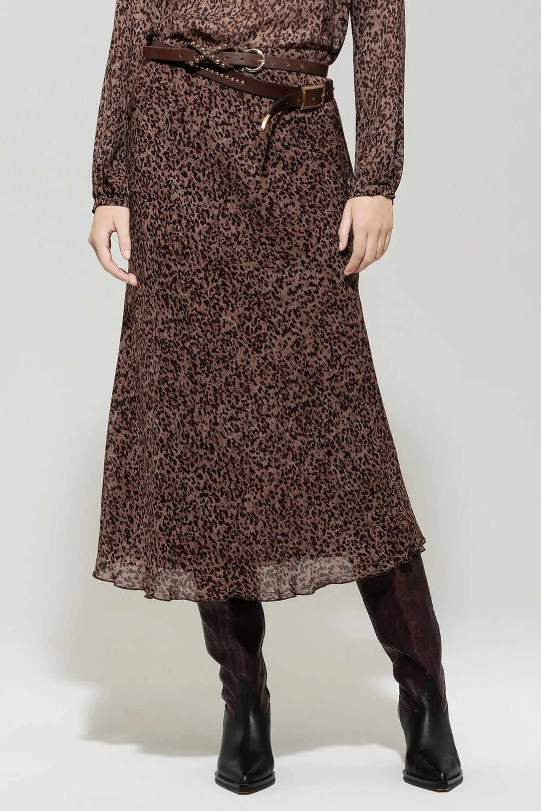 Person wearing a brown leopard print dress with a belt and black knee-high boots on a white background