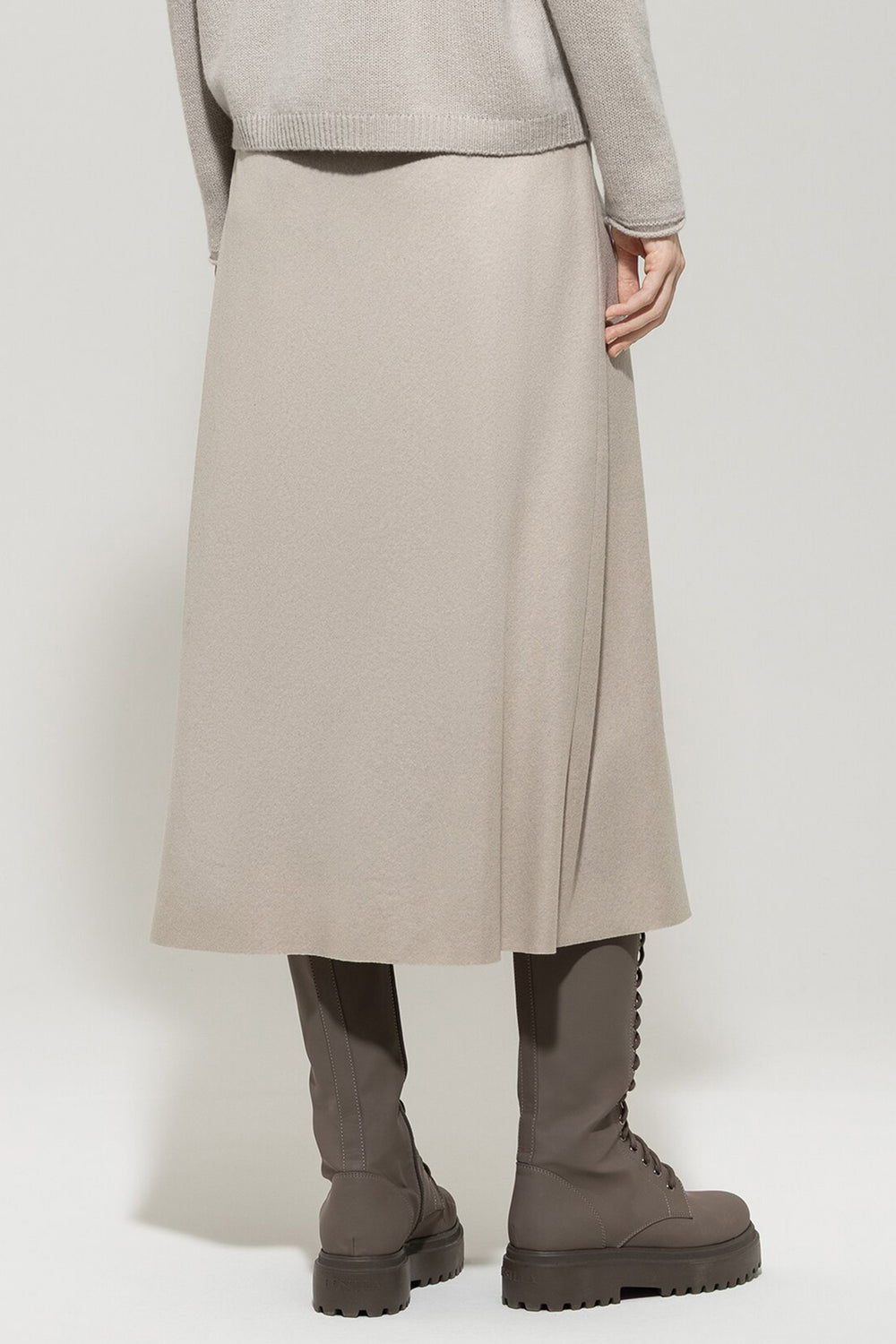 Person wearing a beige skirt, sweater, and boots on a white background