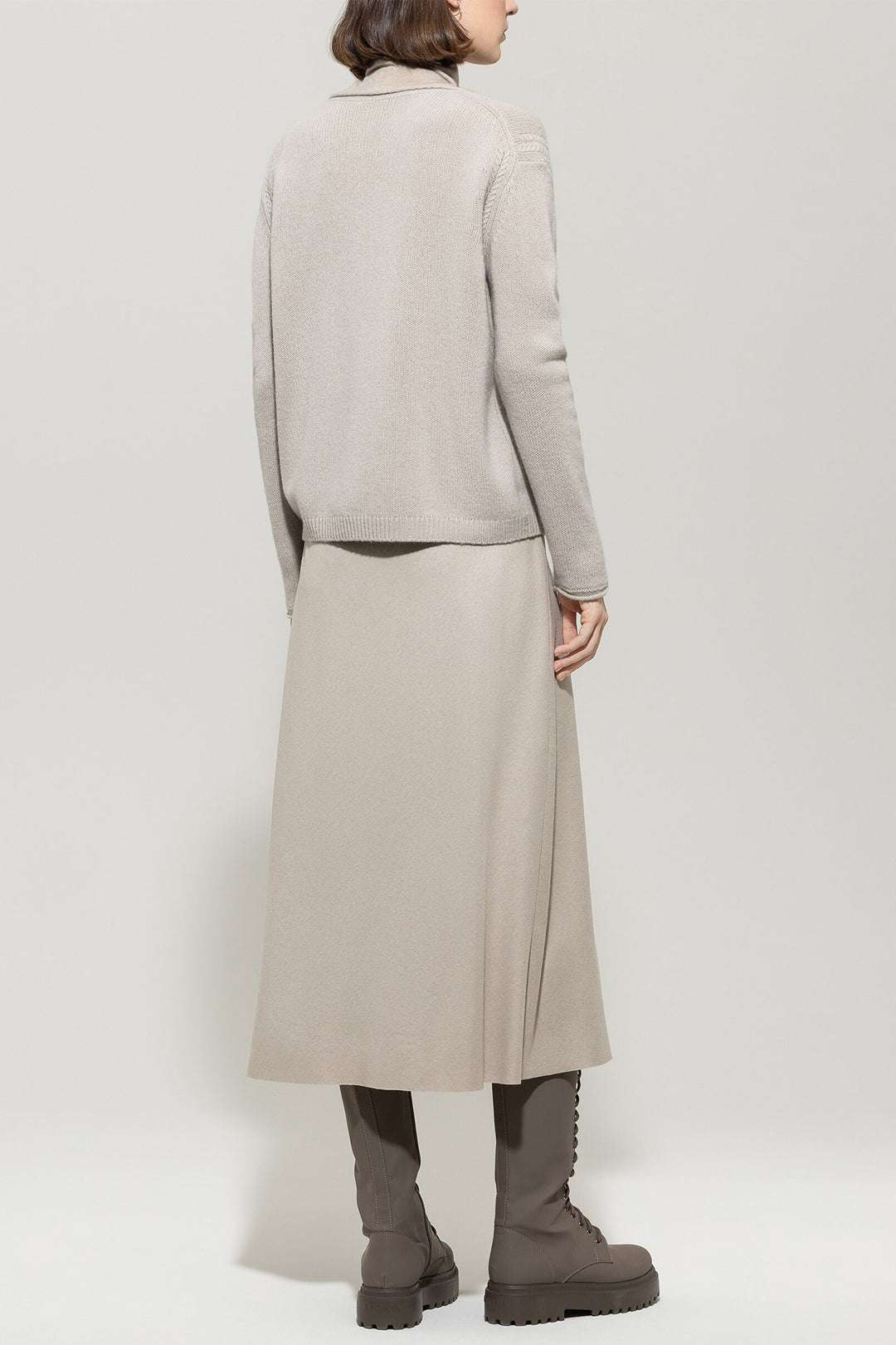 Person wearing a beige coat and pants with brown boots on a white background