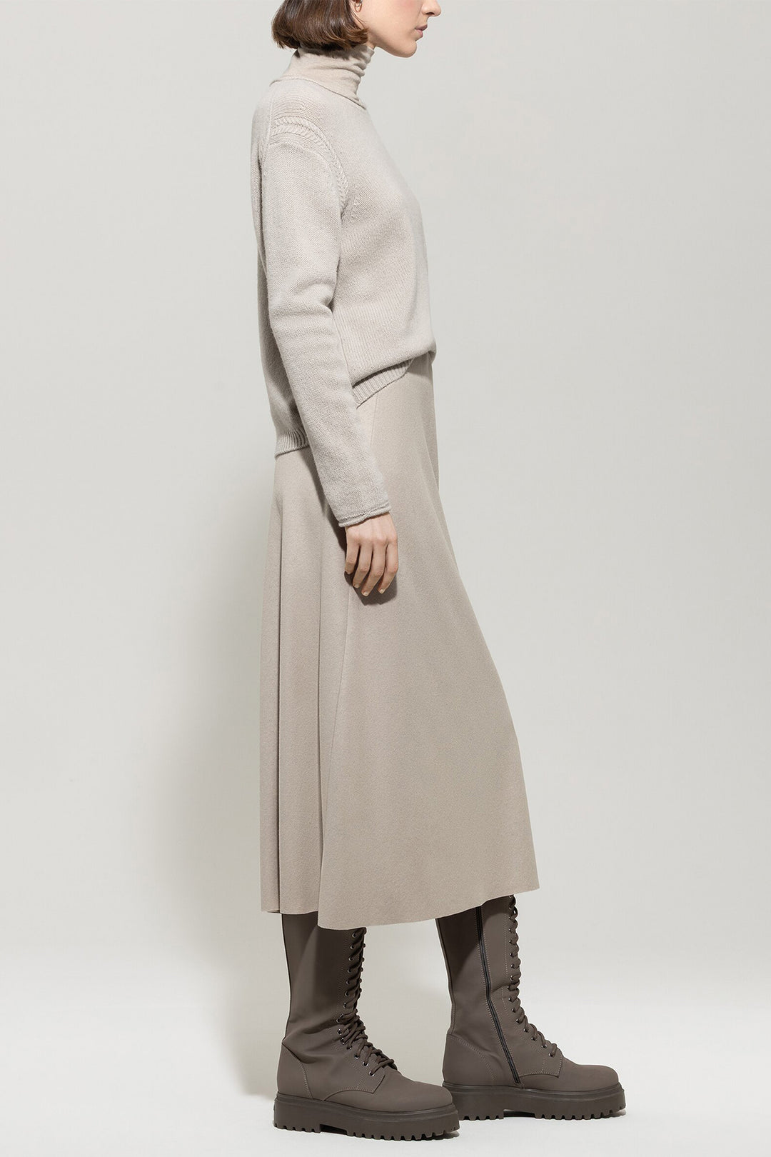 Person wearing a long beige coat and brown boots on a white background