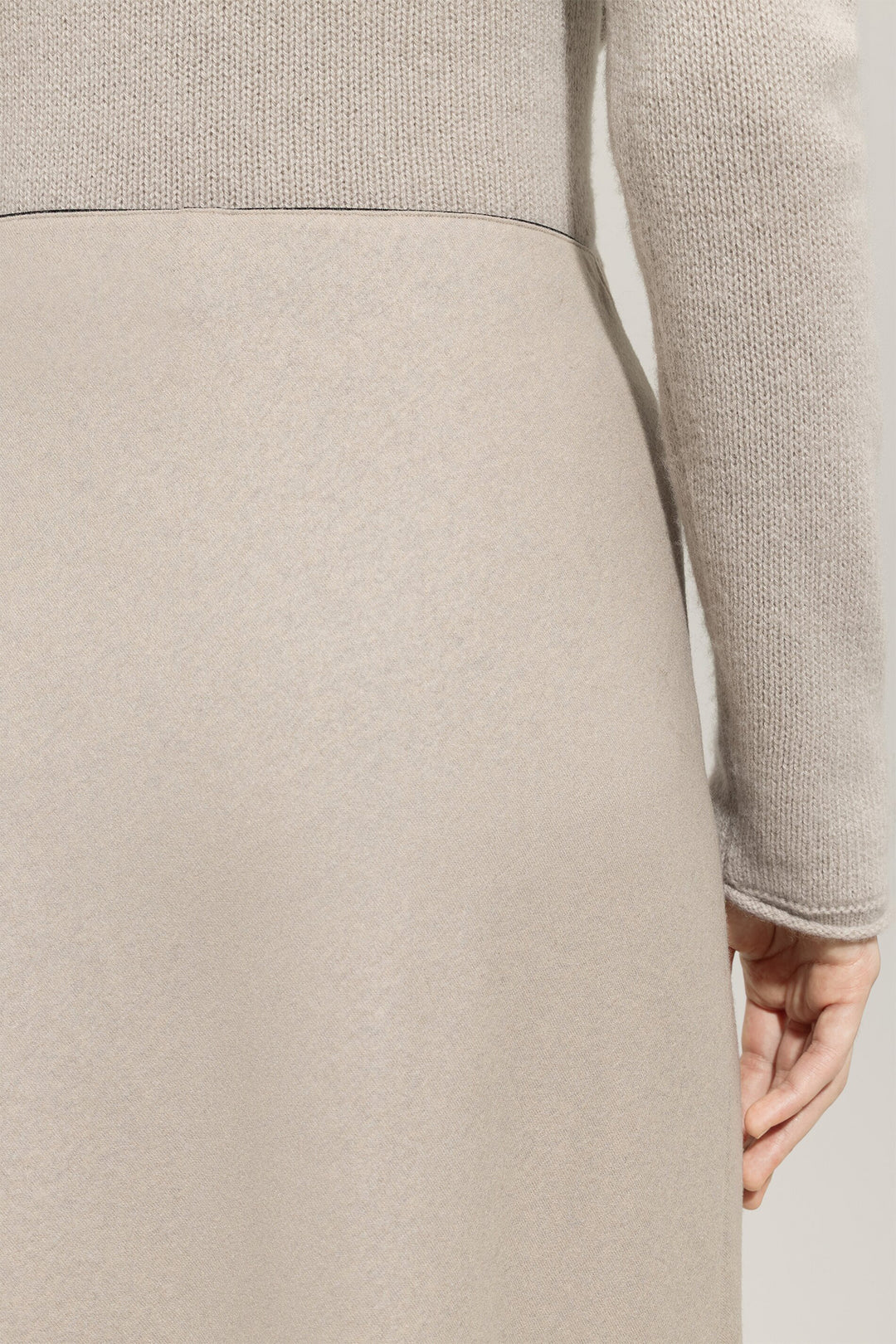 Close-up of a person wearing a light gray sweater and beige skirt against a neutral background