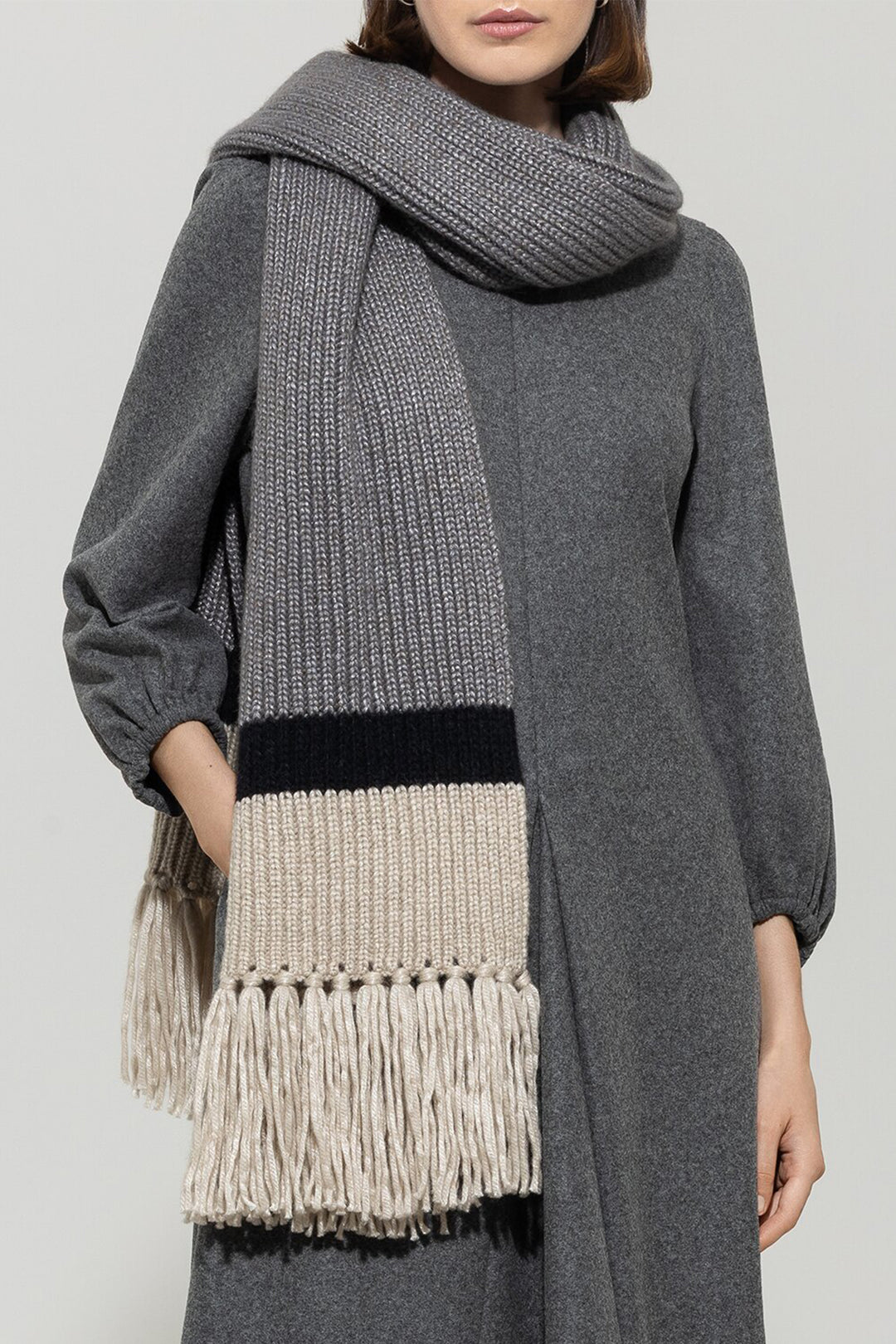 Person wearing a gray scarf with fringe details on a plain background