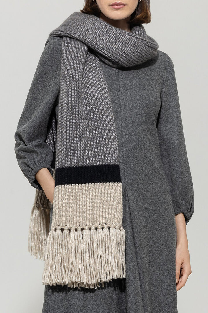 Person wearing a gray scarf with fringe details on a plain background