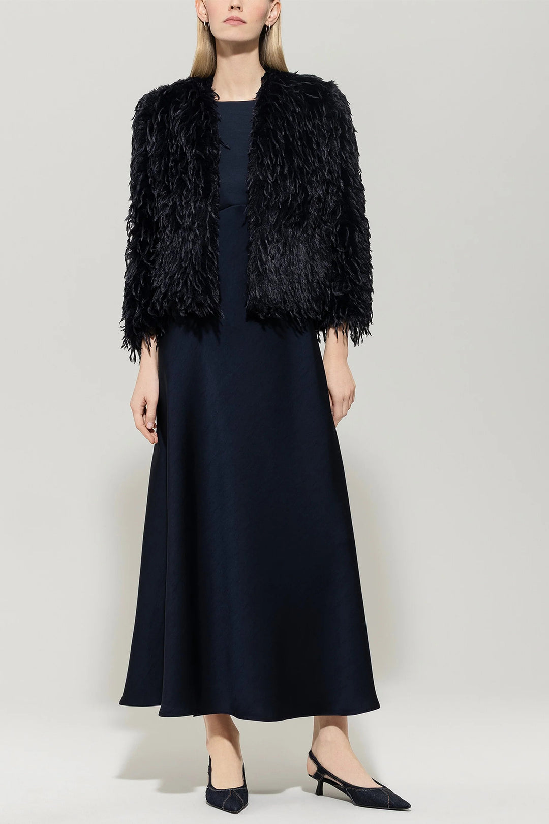 Woman wearing a navy fur vest over a navy dress on a plain background