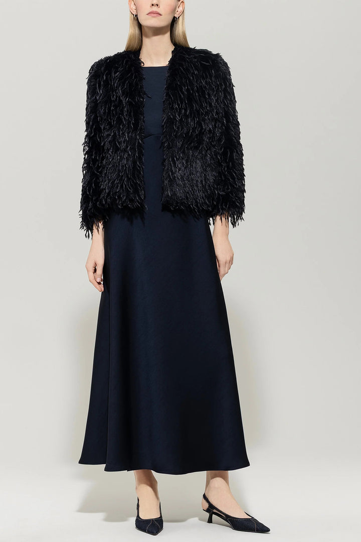 Woman wearing a navy fur vest over a navy dress on a plain background