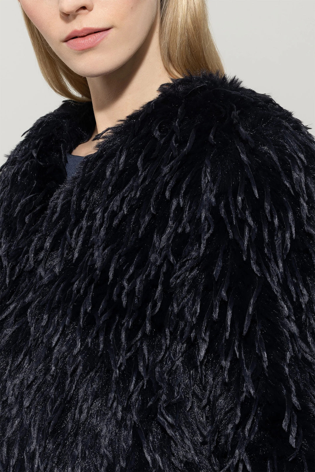 Close-up of a person wearing a navy fluffy coat against a neutral background
