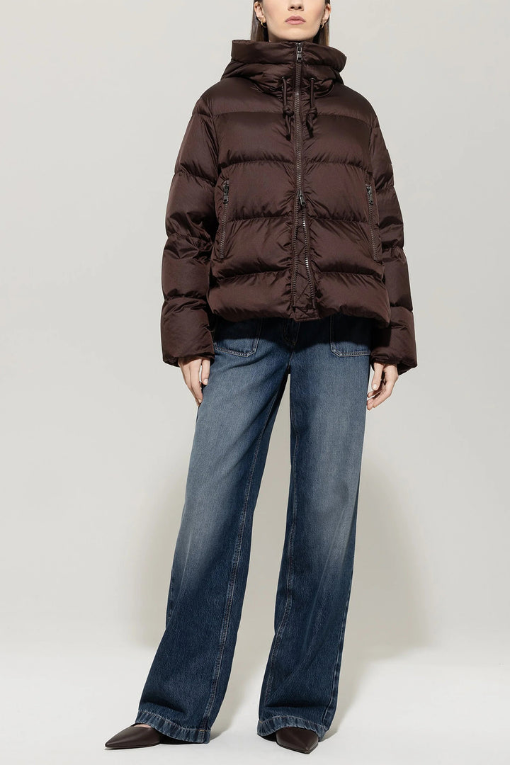 Person wearing a brown puffer jacket and blue jeans on a white background