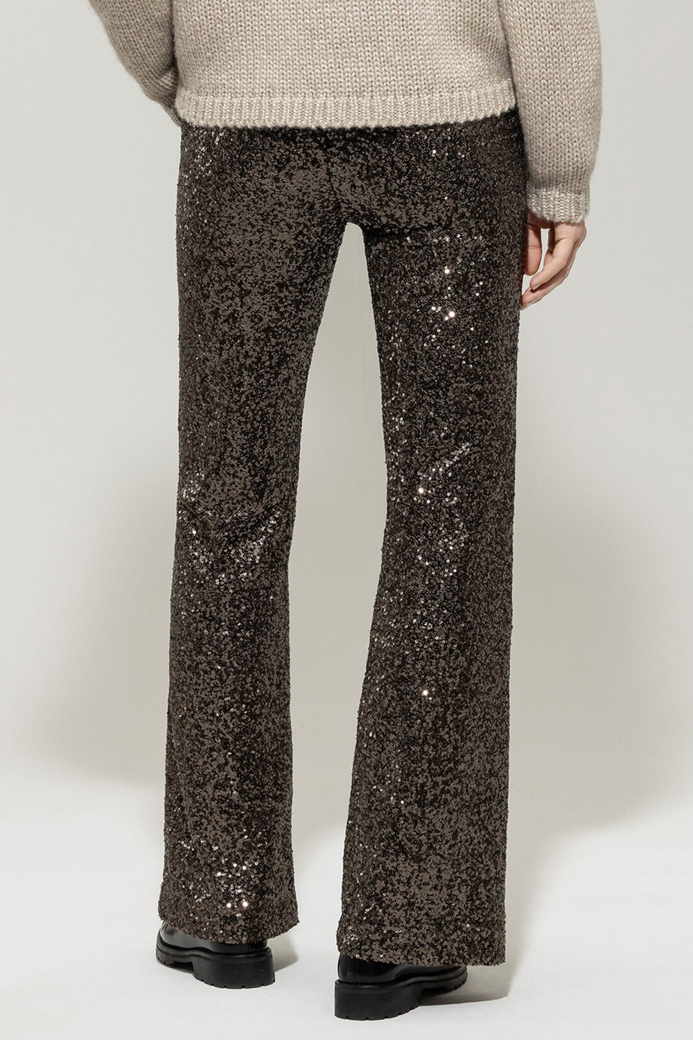 Person wearing sparkly black pants and a beige sweater on a white background
