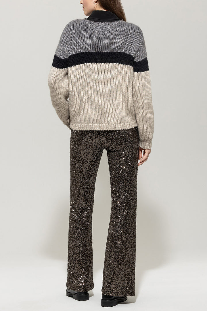 Person wearing a gray and black sweater with sequin pants on a white background